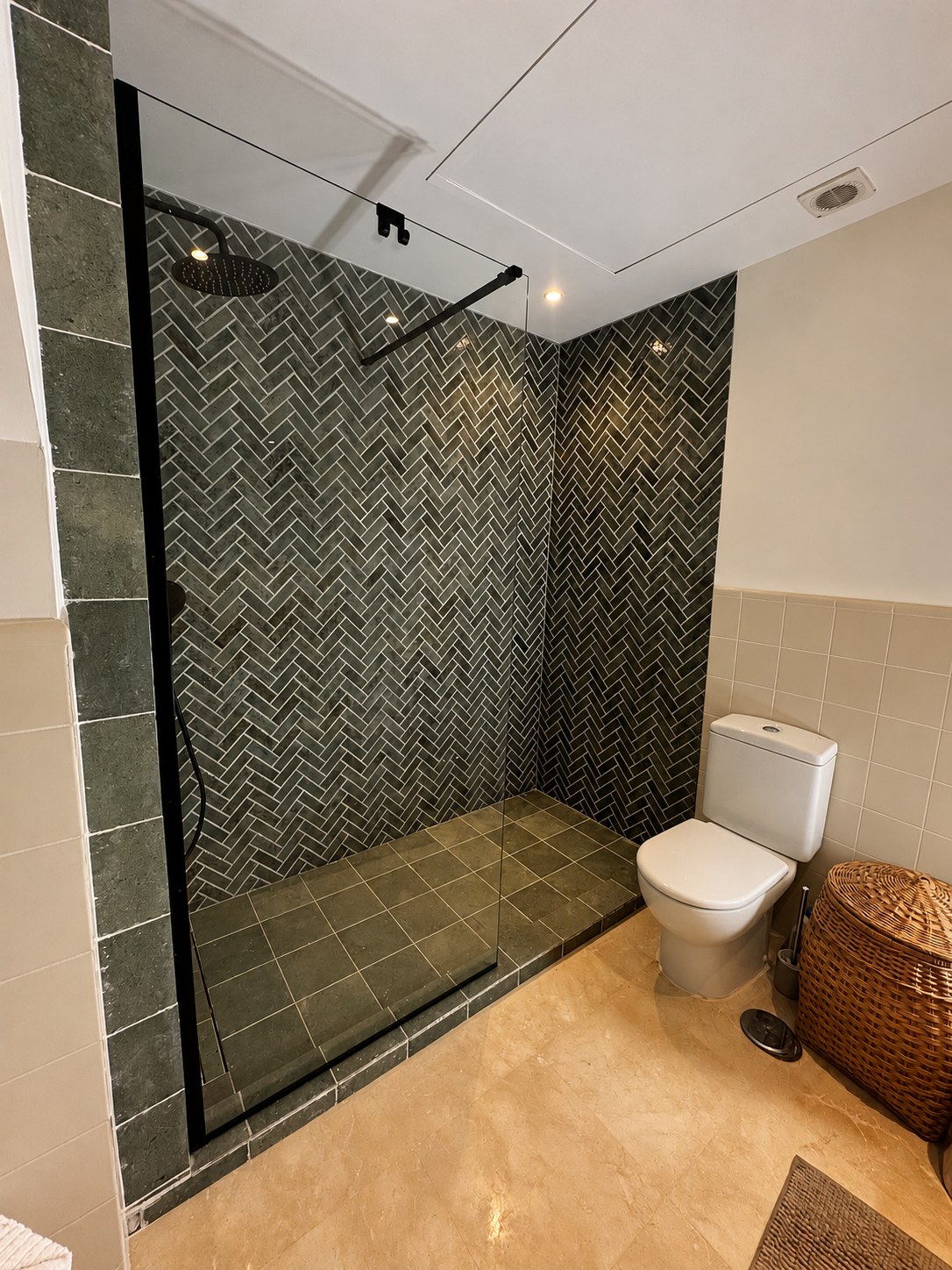 Renovated bathroom with a walk-in shower, green herringbone tiles and a black glass screen